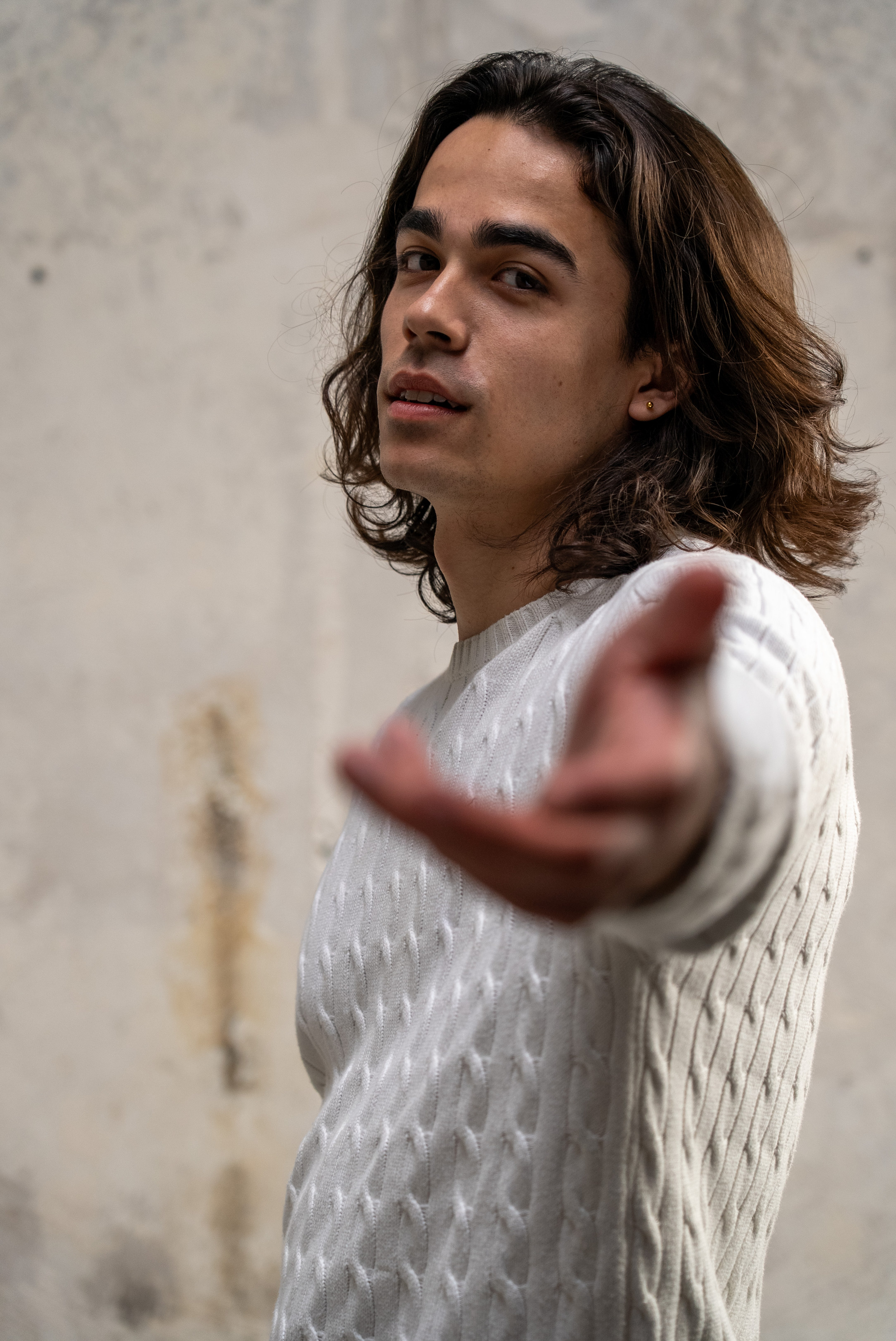 Portrait d’un comédien en pull blanc tendant la main vers l’objectif, réalisé en studio dans une lumière douce.