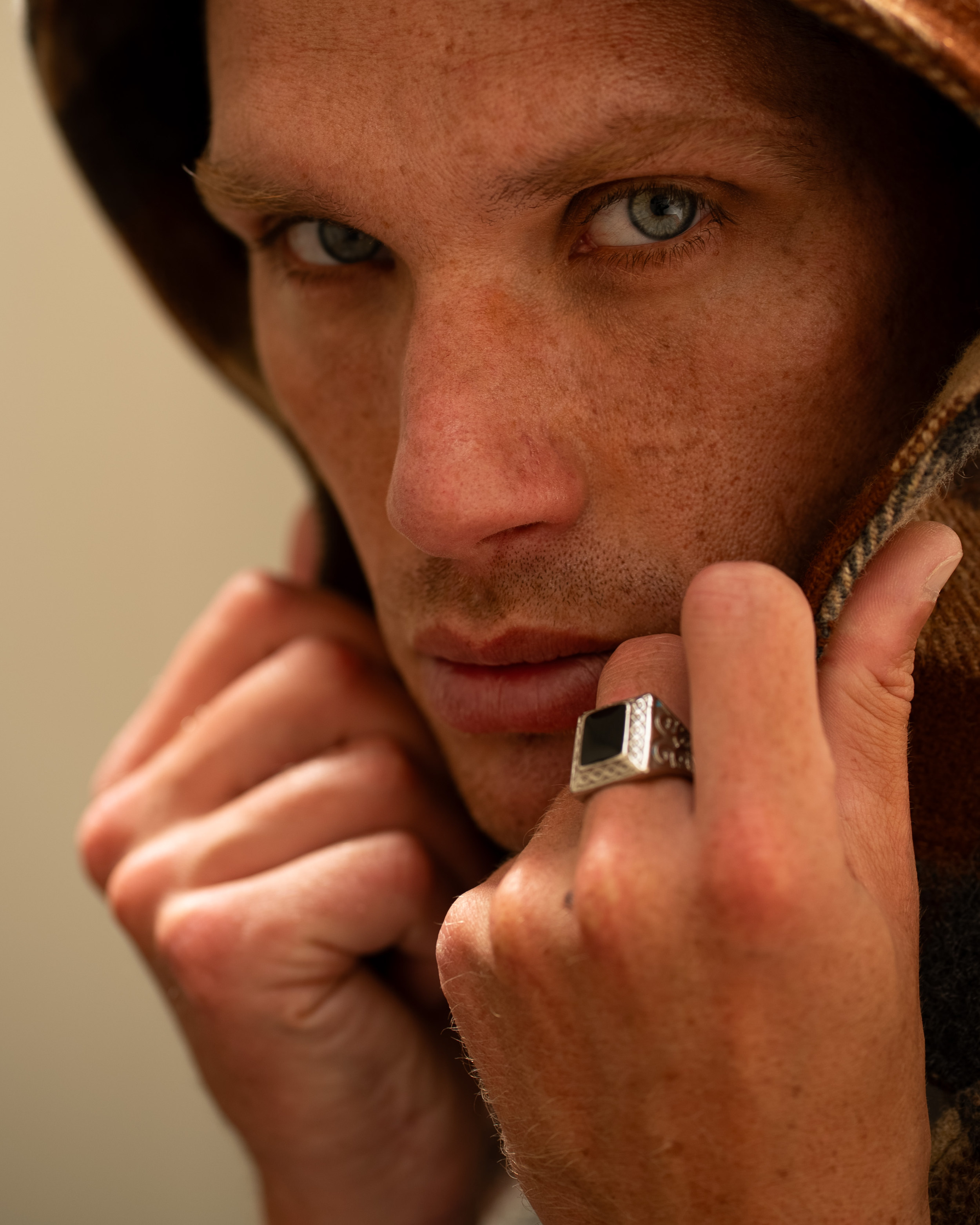 Portrait serré d’un mannequin homme regardant l’objectif, éclairé en lumière naturelle, capuche relevée autour du visage.