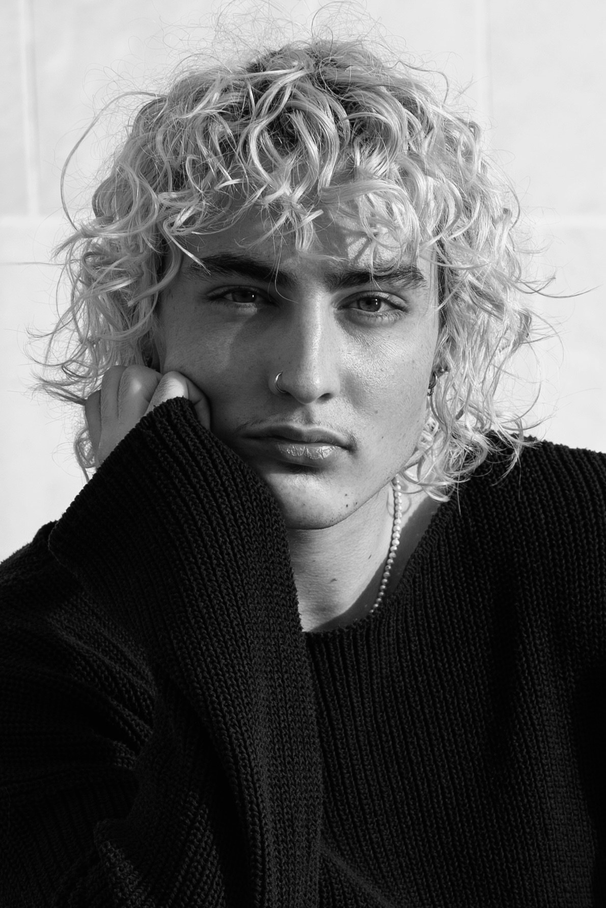 Portrait en noir et blanc d’un homme aux cheveux bouclés photographié en lumière naturelle.