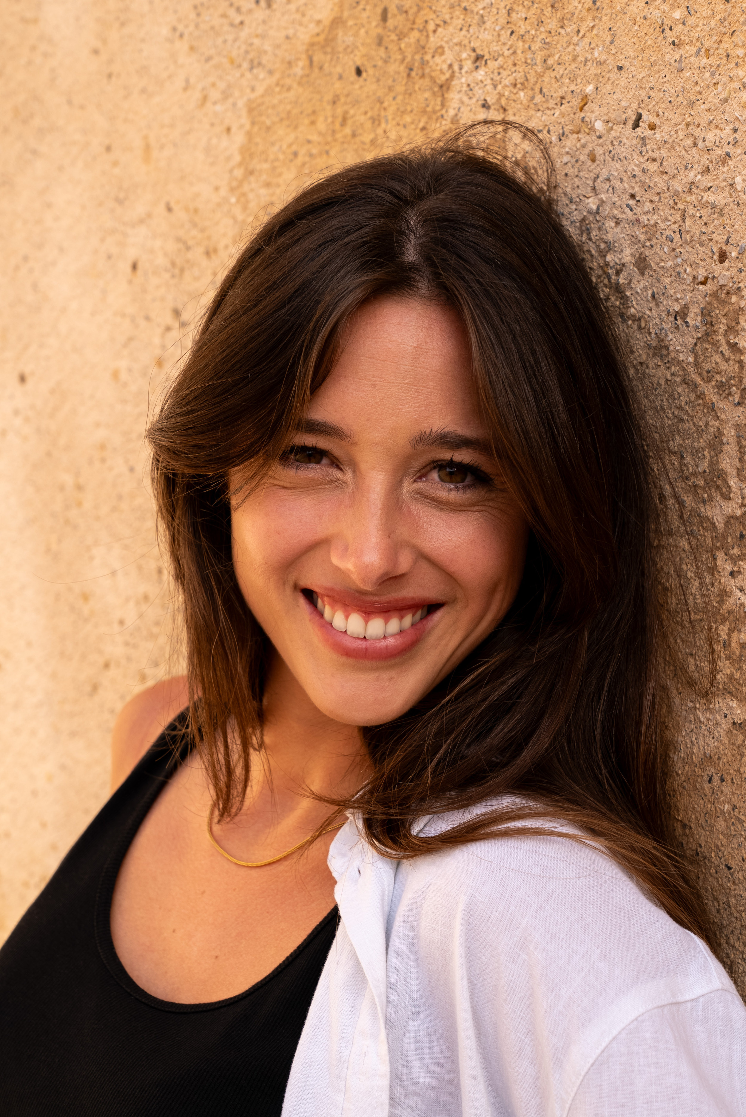 Portrait naturel d’une femme souriante en lumière naturelle contre un mur à Marseille.
