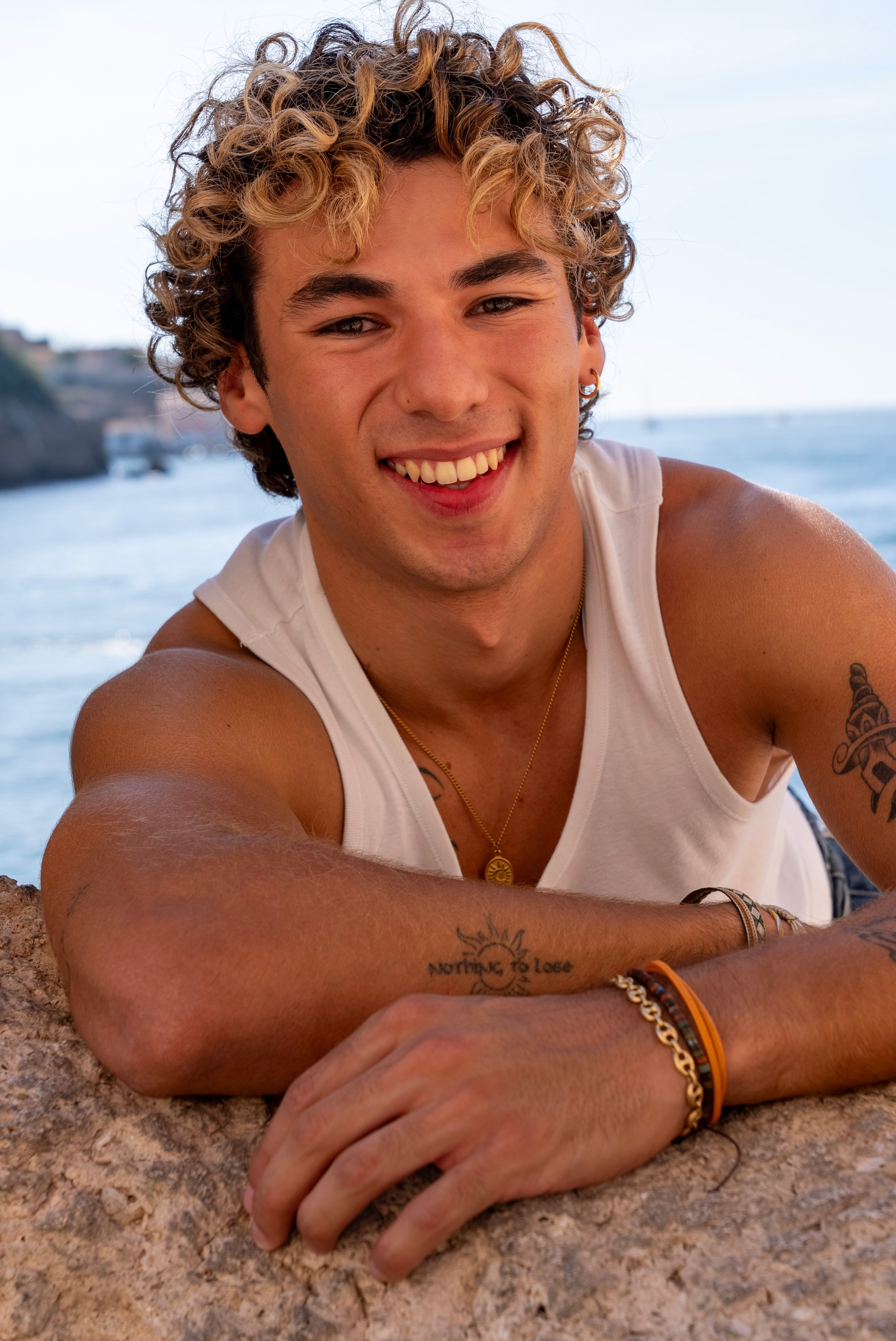 Portrait lifestyle d’un jeune homme souriant photographié en lumière naturelle au bord de la mer à Marseille.