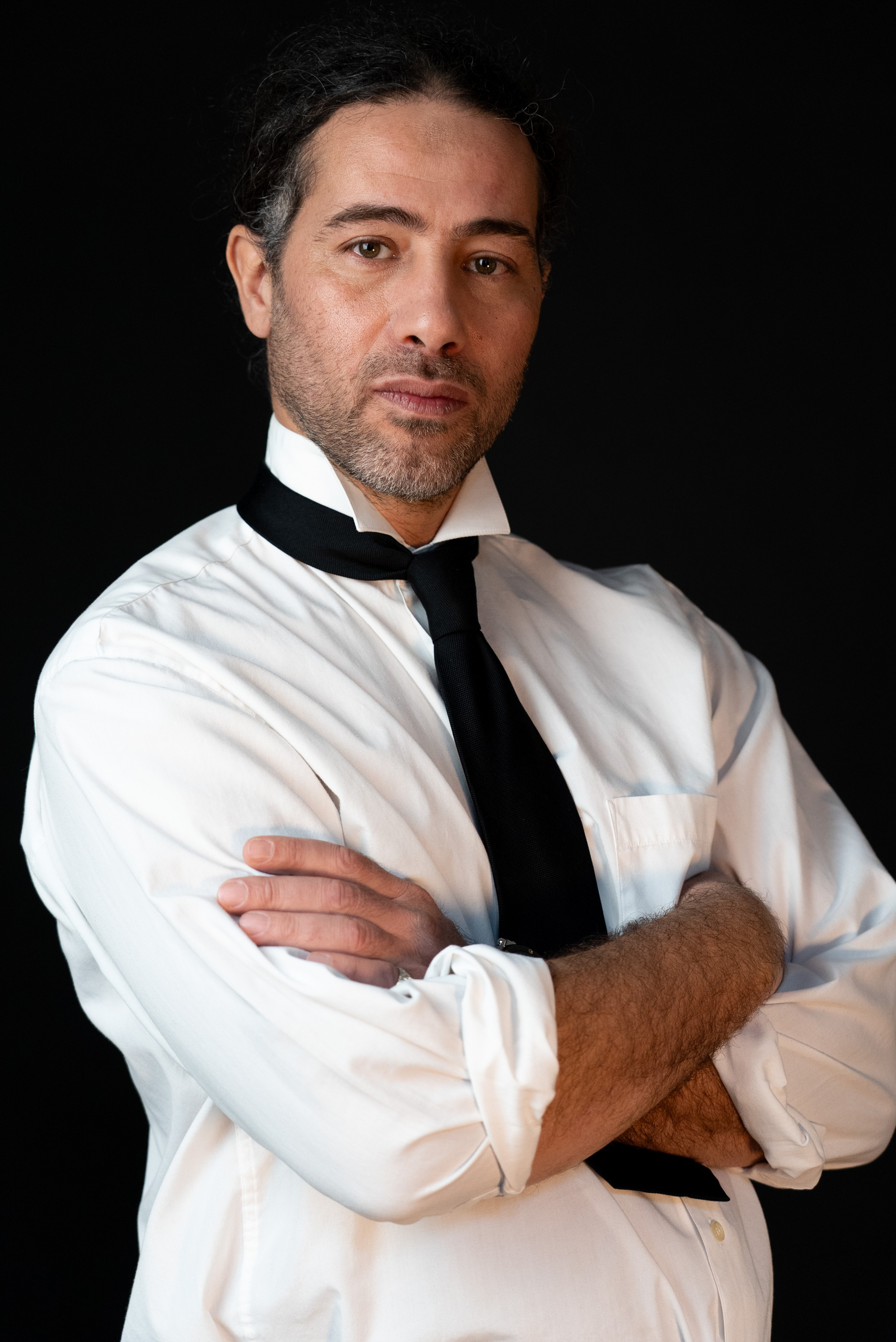 Portrait professionnel d’un homme en chemise blanche et cravate, photographié en studio sur fond sombre.