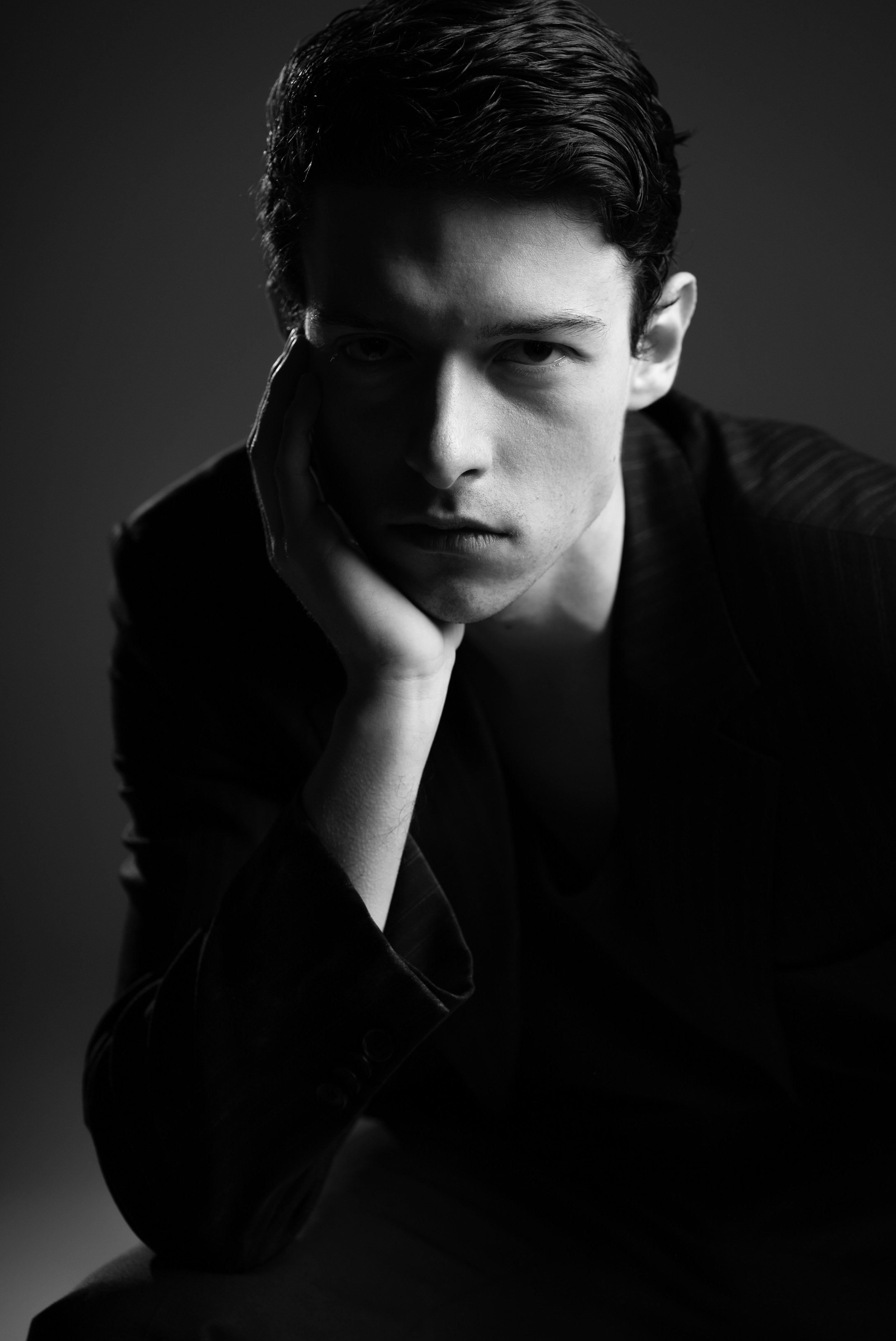 Portrait masculin en studio en clair-obscur avec une lumière dramatique et un fond sombre.